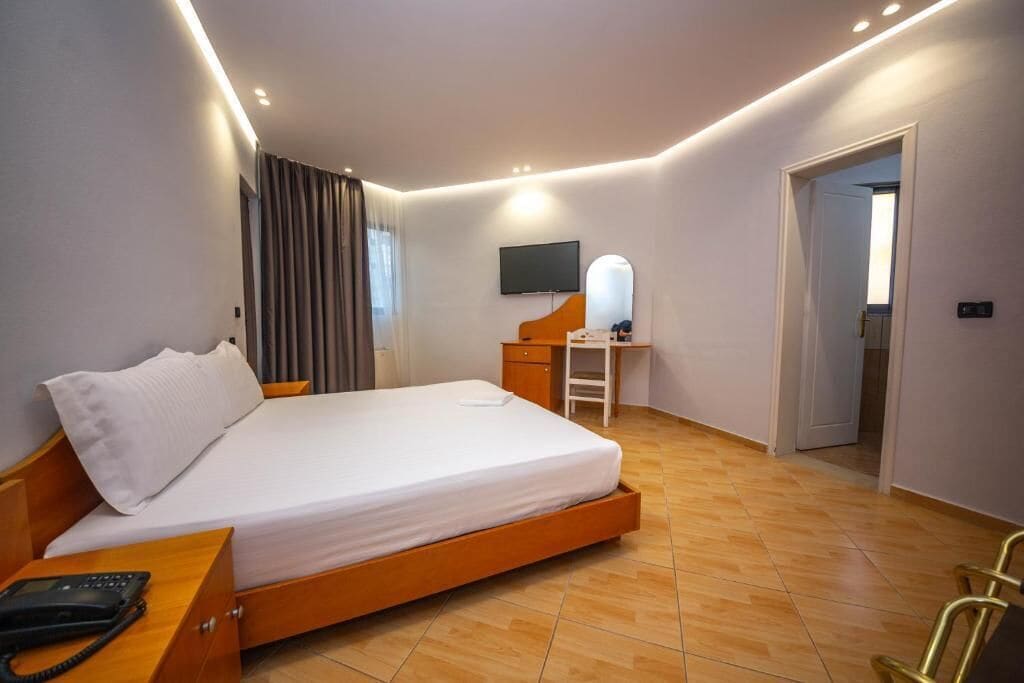 Moderni hotellihuone, jossa on suuri sänky, työpöytä, tuoli, taulutelevisio ja puhelin.