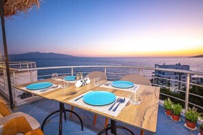 A table set for two with blue plates and cutlery, overlooking a body of water at sunset. - Hotel Sea Breeze (Sarandë)