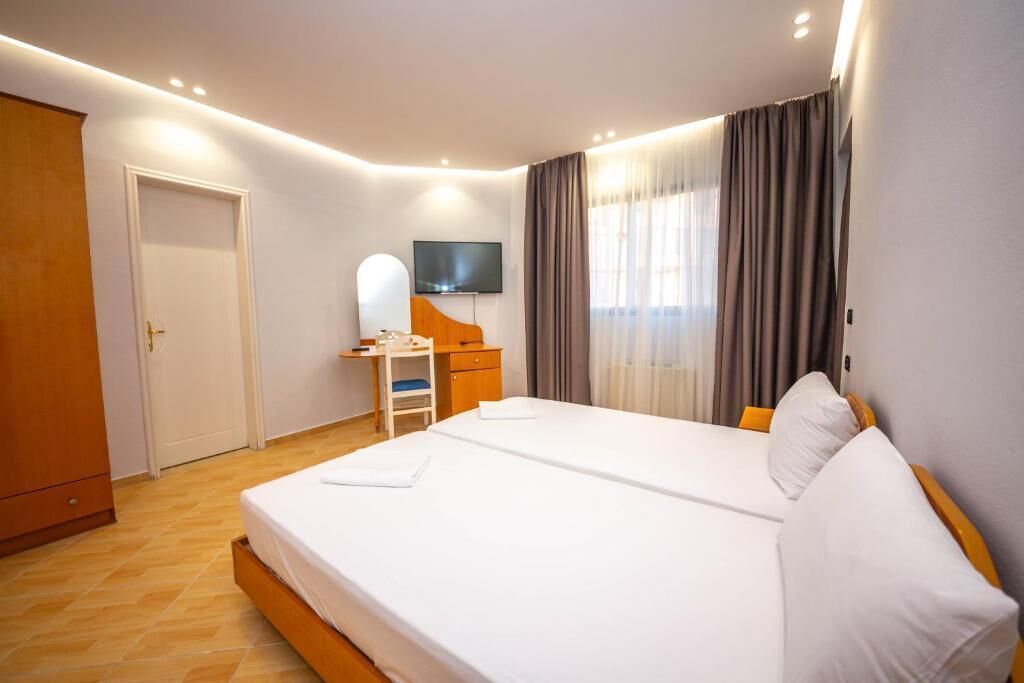 A hotel room with a large bed, a desk with a chair, a television, and a wardrobe.