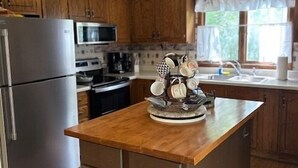 Una cucina con mobili in legno, un'isola centrale, elettrodomestici in acciaio inossidabile e una finestra con tende.