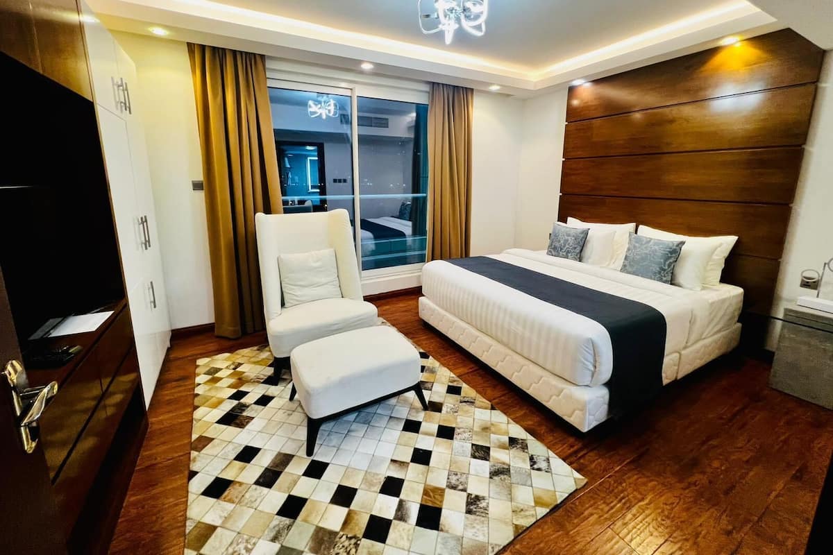 A modern hotel room with a large bed, a seating area, and a view of the city through the window.