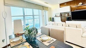 Ein modernes Wohnzimmer mit Essbereich für vier Personen, einer Couch, einem Flachbildfernseher und Blick auf die Stadt.