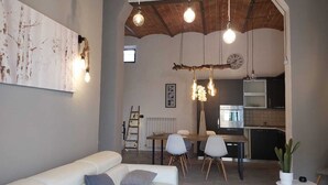 Un salon moderne avec un canapé, une table à manger et des chaises. On aperçoit au fond une cuisine équipée d’un réfrigérateur et d’une cuisinière.