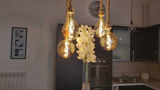 Une cuisine équipée d’appareils modernes, une horloge au mur et des luminaires décoratifs suspendus au plafond.