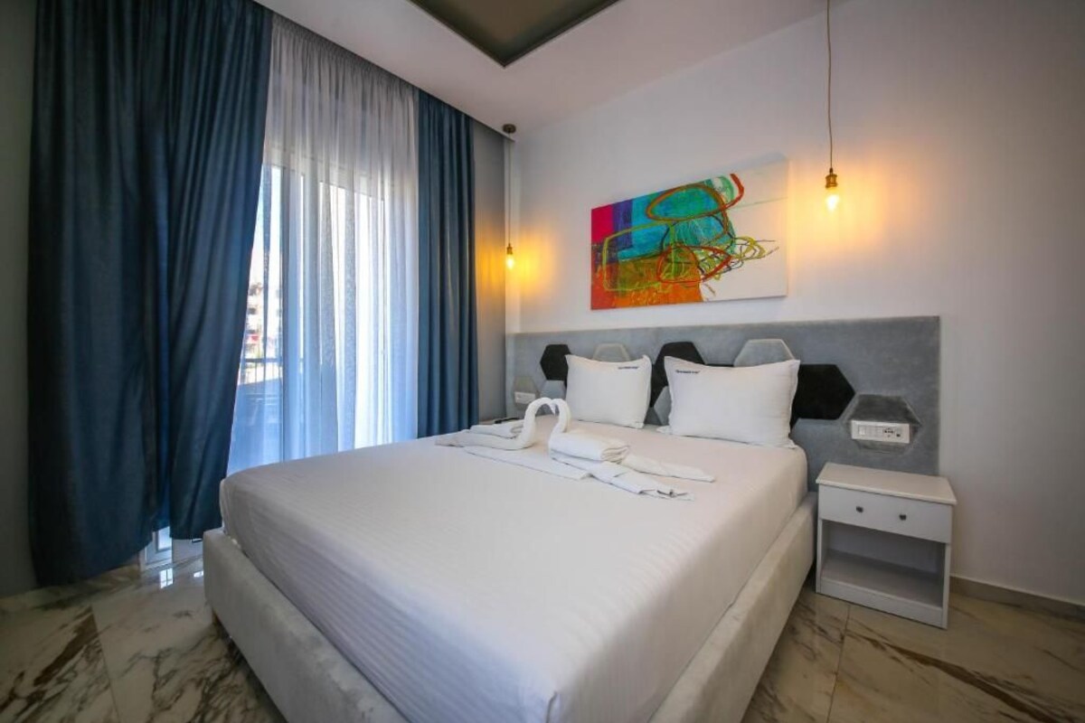 A hotel room with a bed, a nightstand, a painting, and a window with curtains.