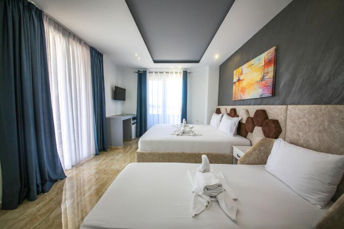 A hotel room with two beds, a desk, a TV, and a painting on the wall.