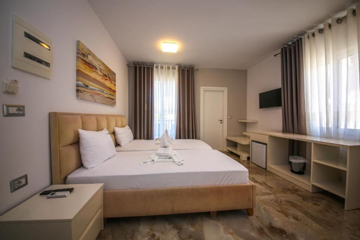 A hotel room with a bed, bedside tables, a TV, and a desk.