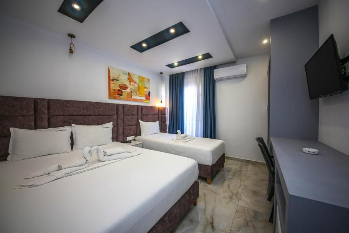 A hotel room with two beds, a desk, a flat-screen TV, and an air conditioning unit.