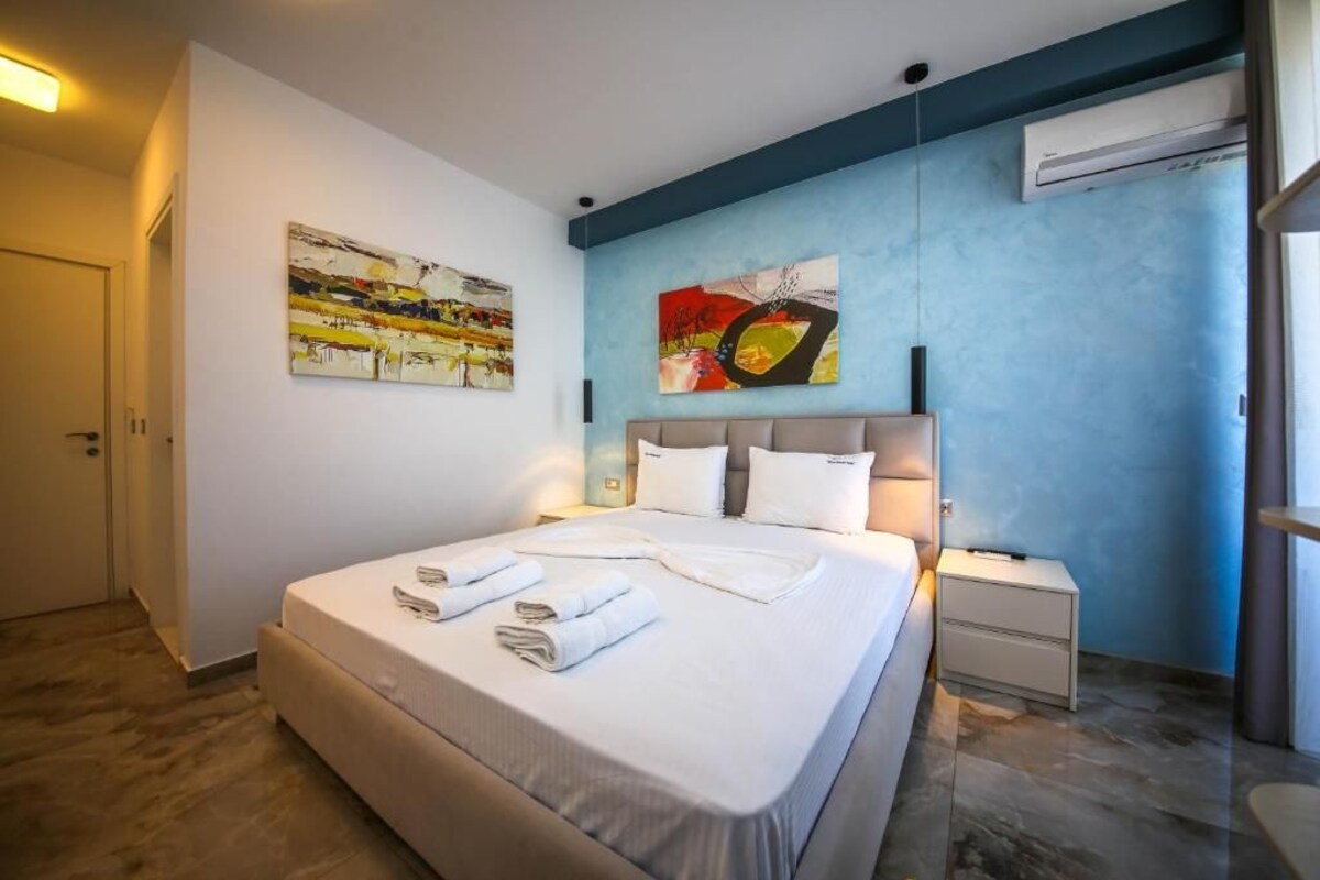 A hotel room with a large bed, a bedside table, a nightstand, and two wall-mounted air conditioning units.