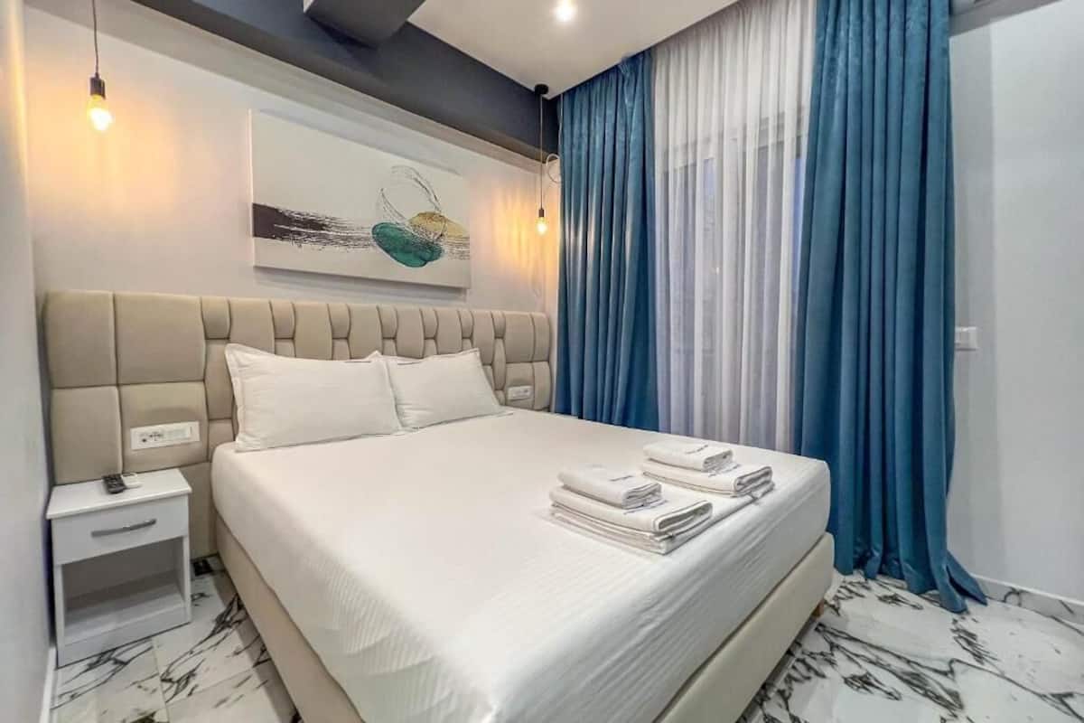 Una habitación de hotel moderna con una cama grande, una mesita de noche con lámpara y un cuadro en la pared.