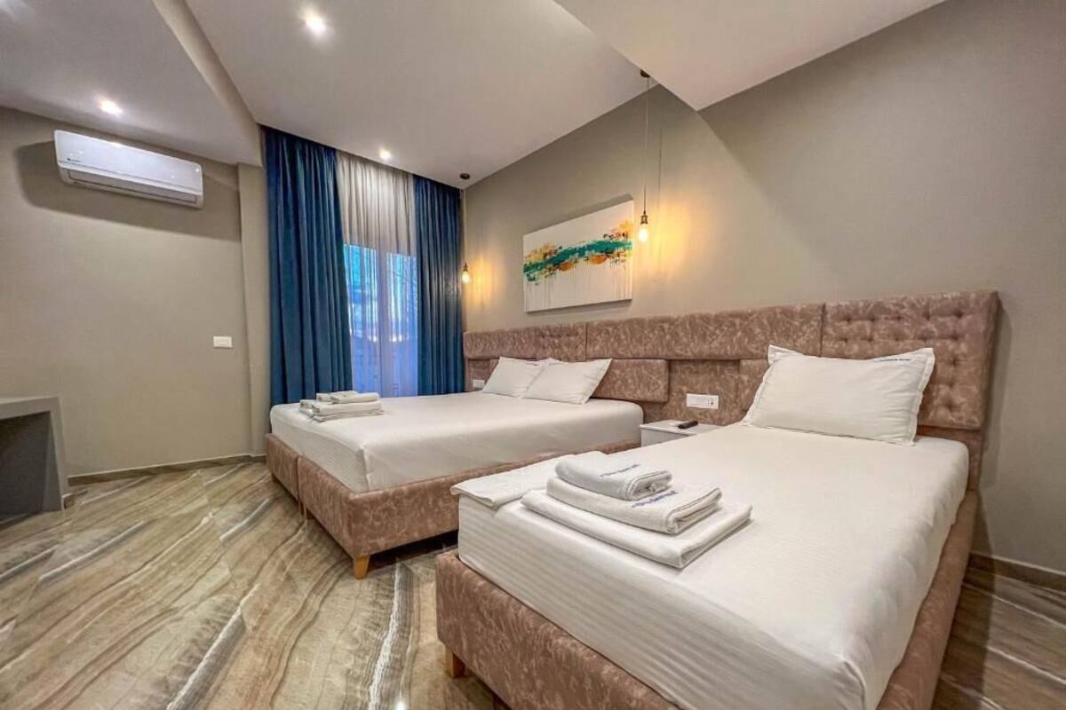 Habitación de hotel con dos camas, un ventanal con cortinas azules, un equipo de aire acondicionado y una lámpara moderna.