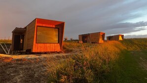 Eine Reihe aus Holzbungalows mit großen Fenstern, eingebettet in eine Wiese unter blauem Himmel.