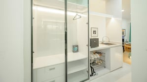 Un bany modern amb una cabina de dutxa de vidre, un lavabo blanc amb mirall i una petita estant amb productes de tocador.