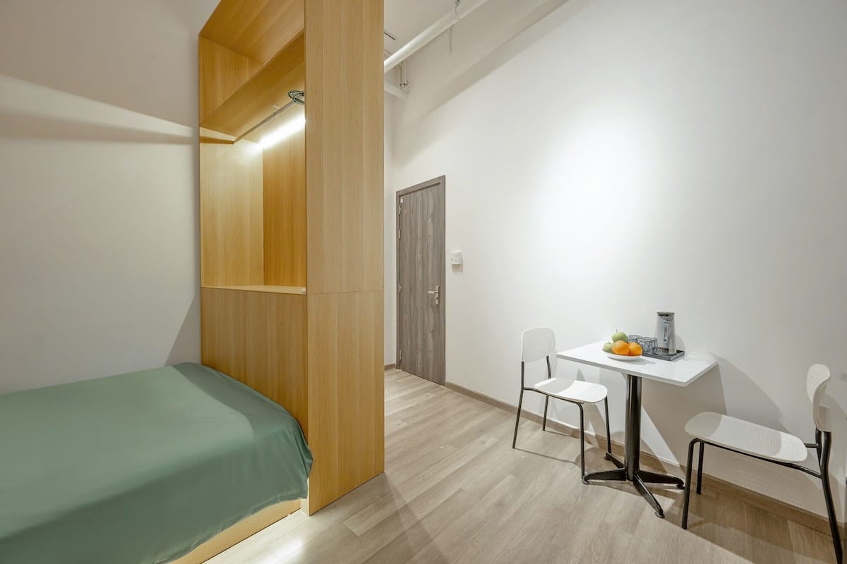 Ein kleiner, moderner Raum mit einem Bett, einem Schreibtisch mit Stühlen und einem Holzschrank.