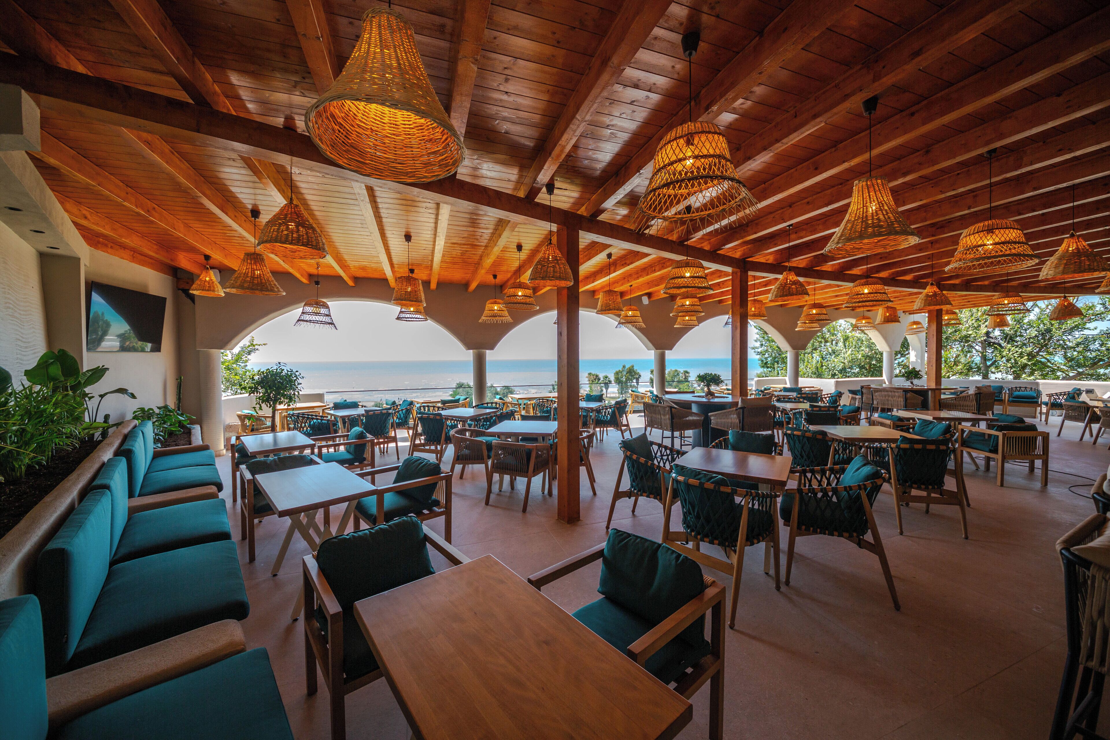 A restaurant with wooden ceiling beams, wicker pendant lights, and outdoor seating with green cushions.