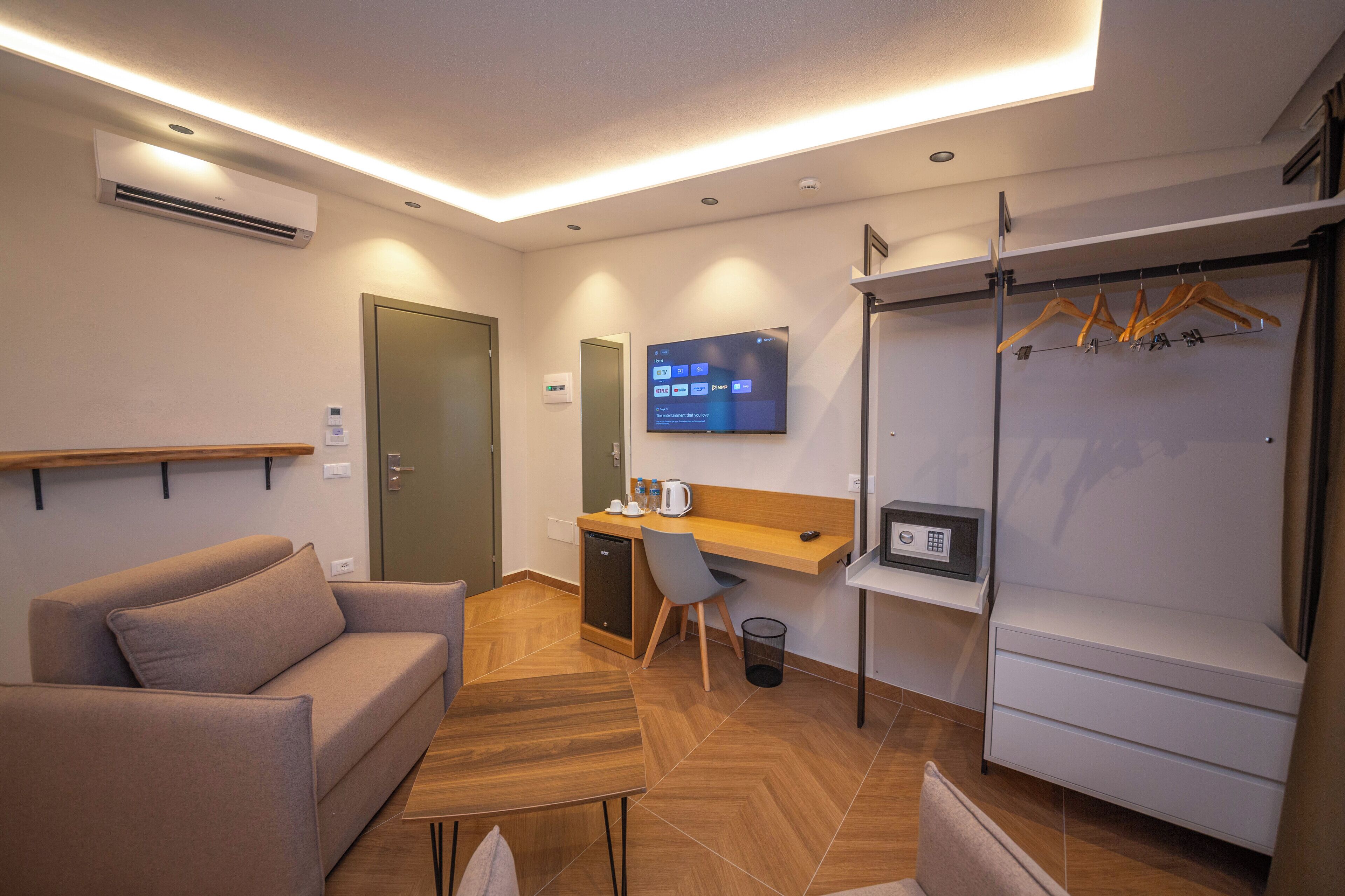 Una habitación de hotel moderna con sofá, escritorio y televisor montado en la pared.