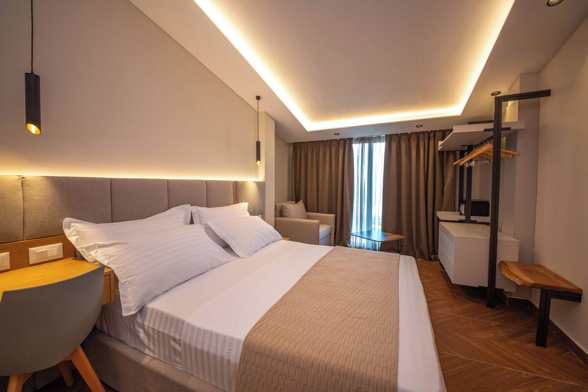 A modern hotel room with a neatly made bed, a desk, a chair, and a small table.