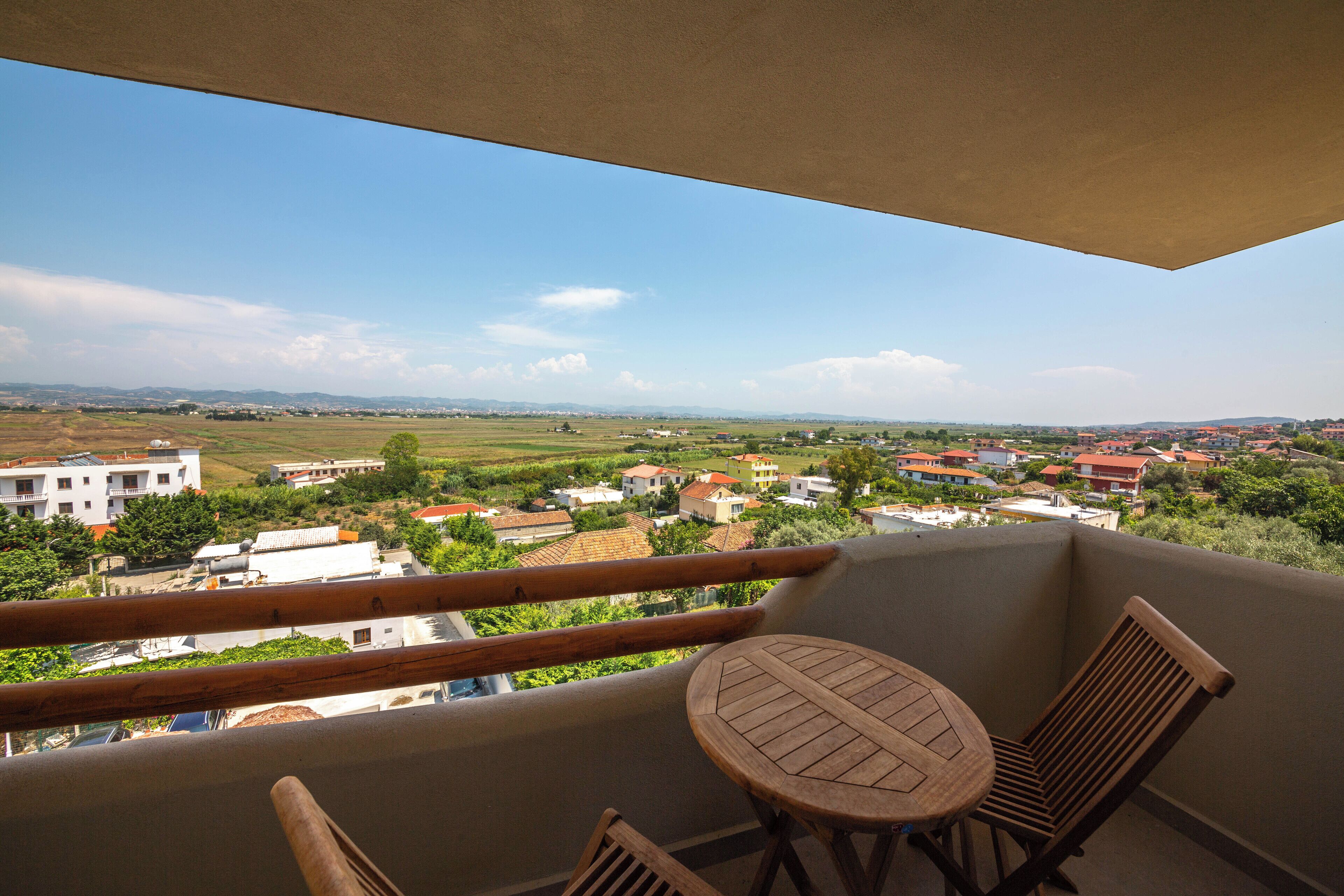 Ein Balkon mit Tisch und Stühlen, der auf einen Wohnbereich mit Häusern und Grünflächen blickt.