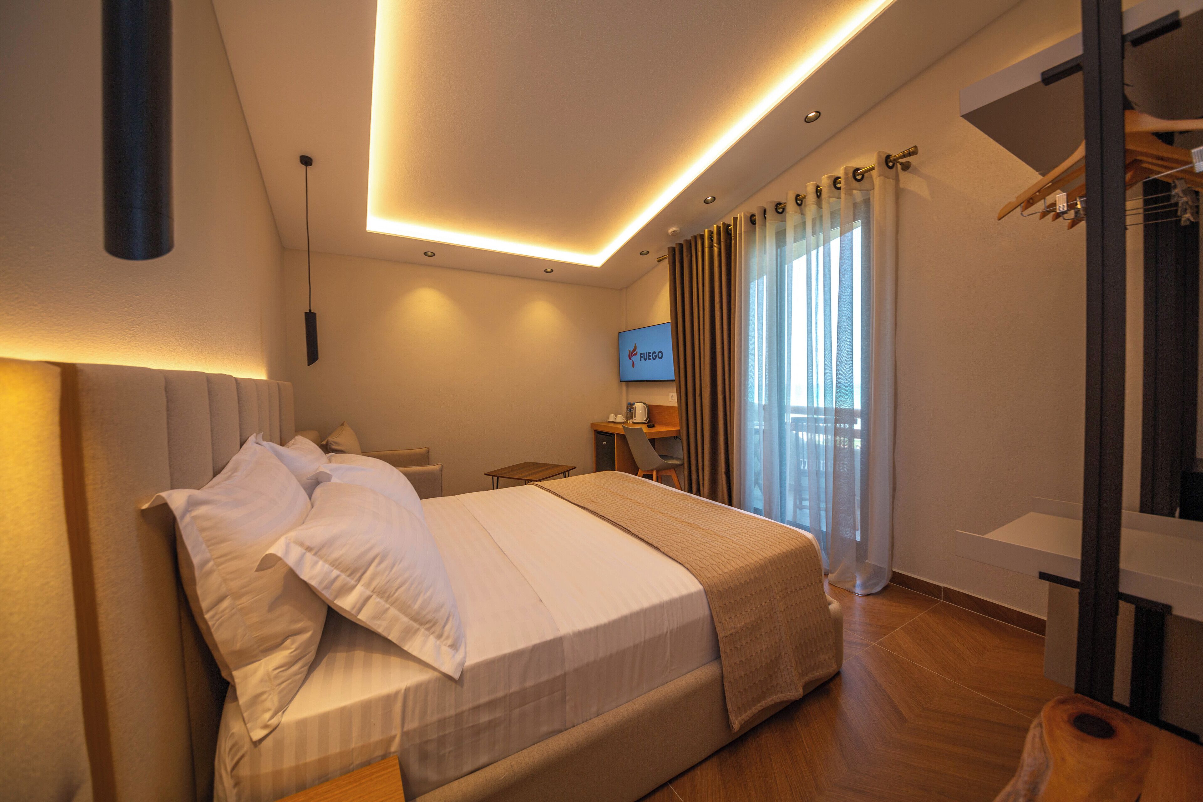 Una habitación de hotel moderna con una cama bien hecha, un escritorio con una silla, un televisor y vistas al exterior a través de amplios ventanales.