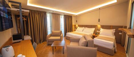A hotel room with a bed, two sofas, a coffee table, a desk with a kettle and cups, and a TV.