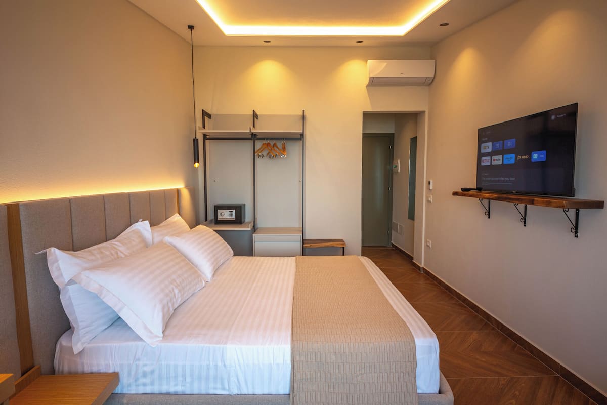 A modern hotel room with a large bed, a TV mounted on the wall, and a wooden shelf.