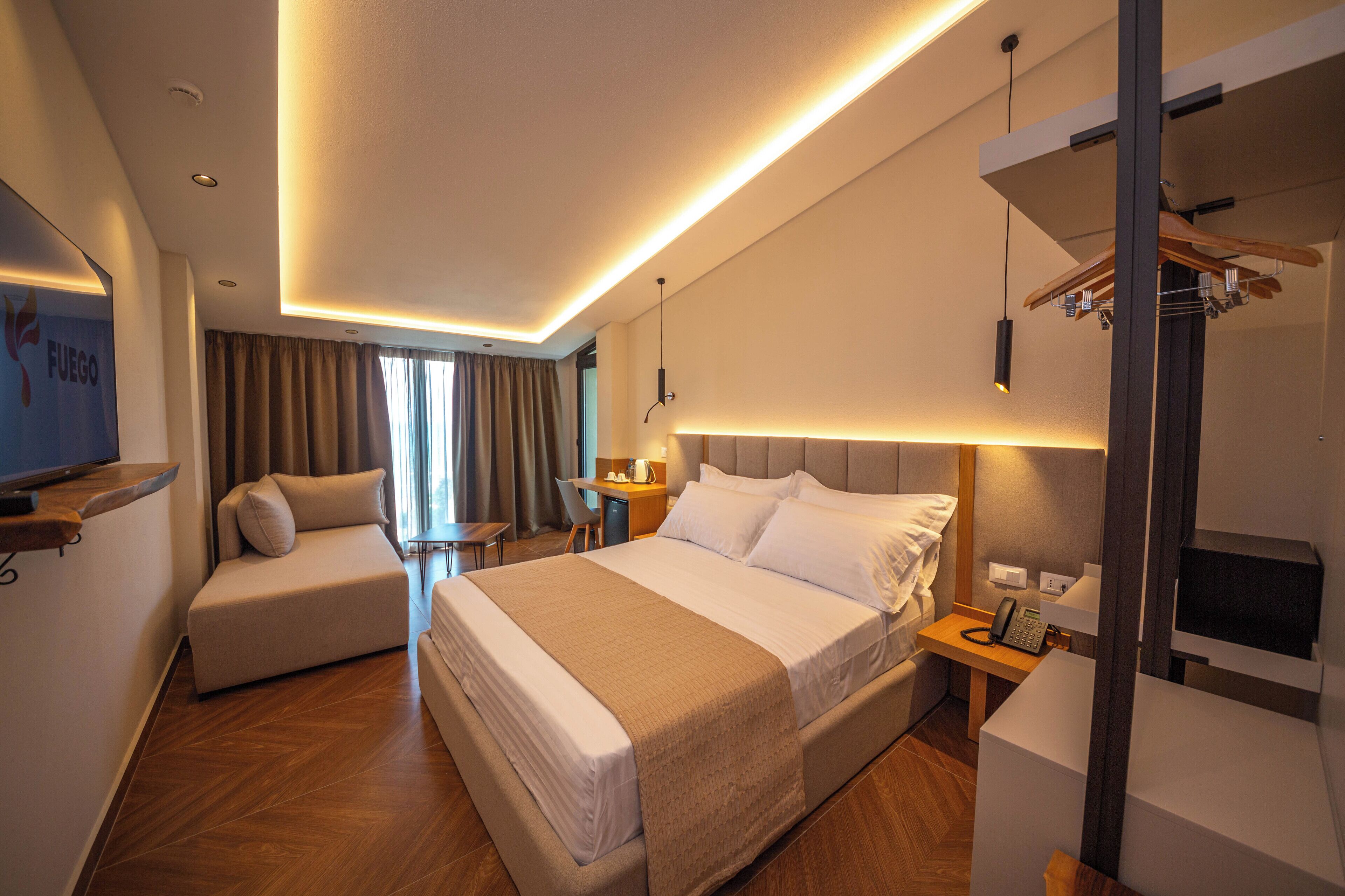 A modern hotel room with a large bed, a seating area, a desk, and a TV.