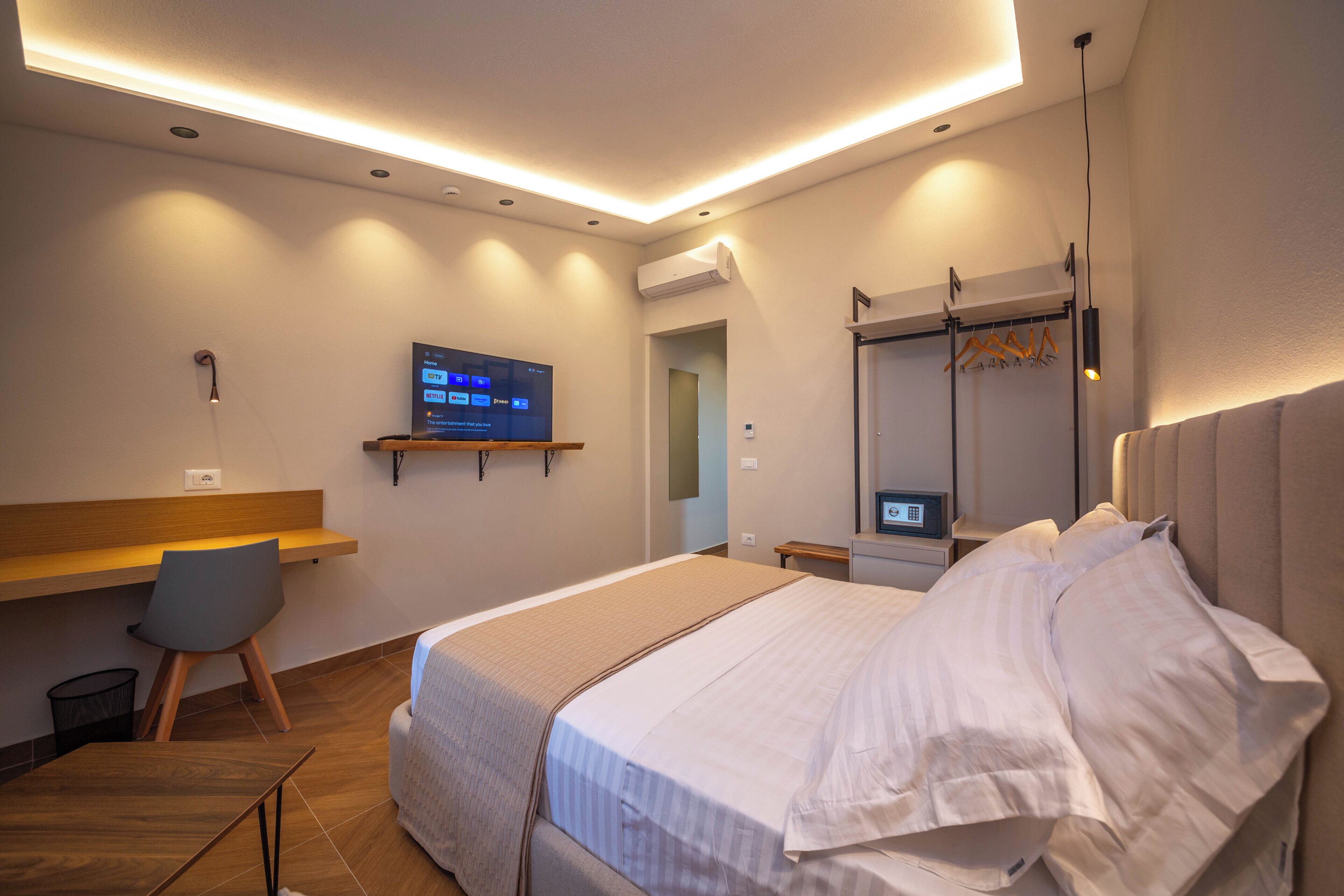 A modern hotel room with a bed, a desk, a chair, a TV, and a wardrobe.