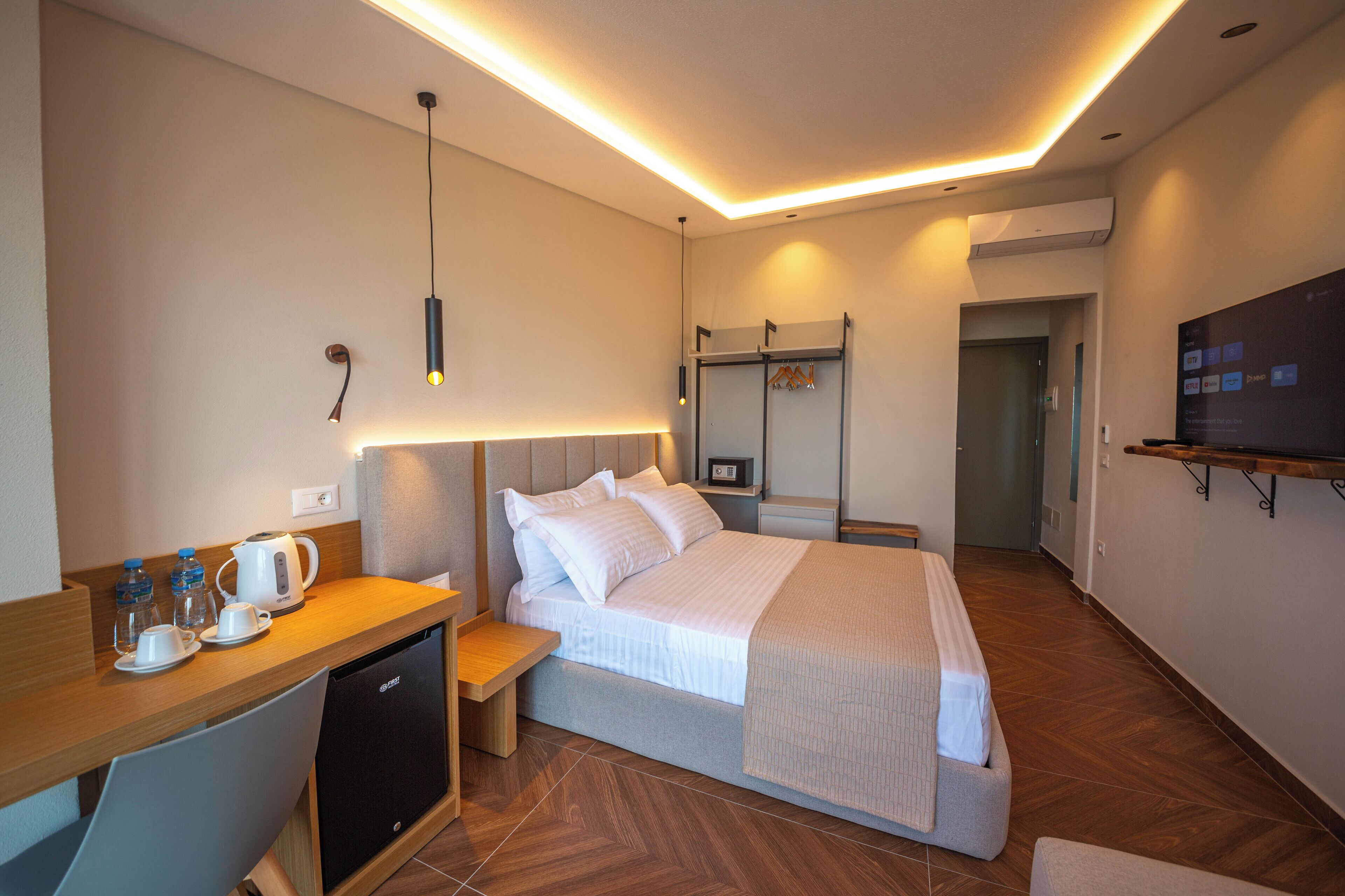 A modern hotel room with a bed, bedside table, and a small desk with a coffee maker and cups.