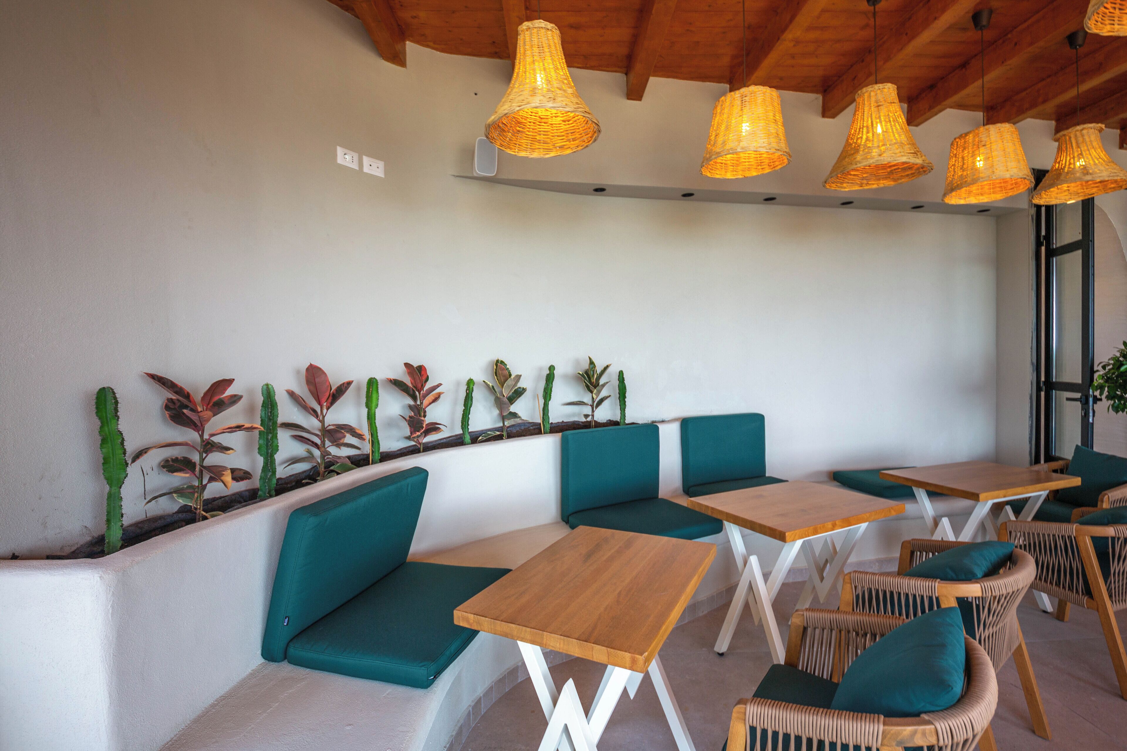 A cafe with wooden tables and green cushioned seating, wicker chairs, and hanging wicker lamps.