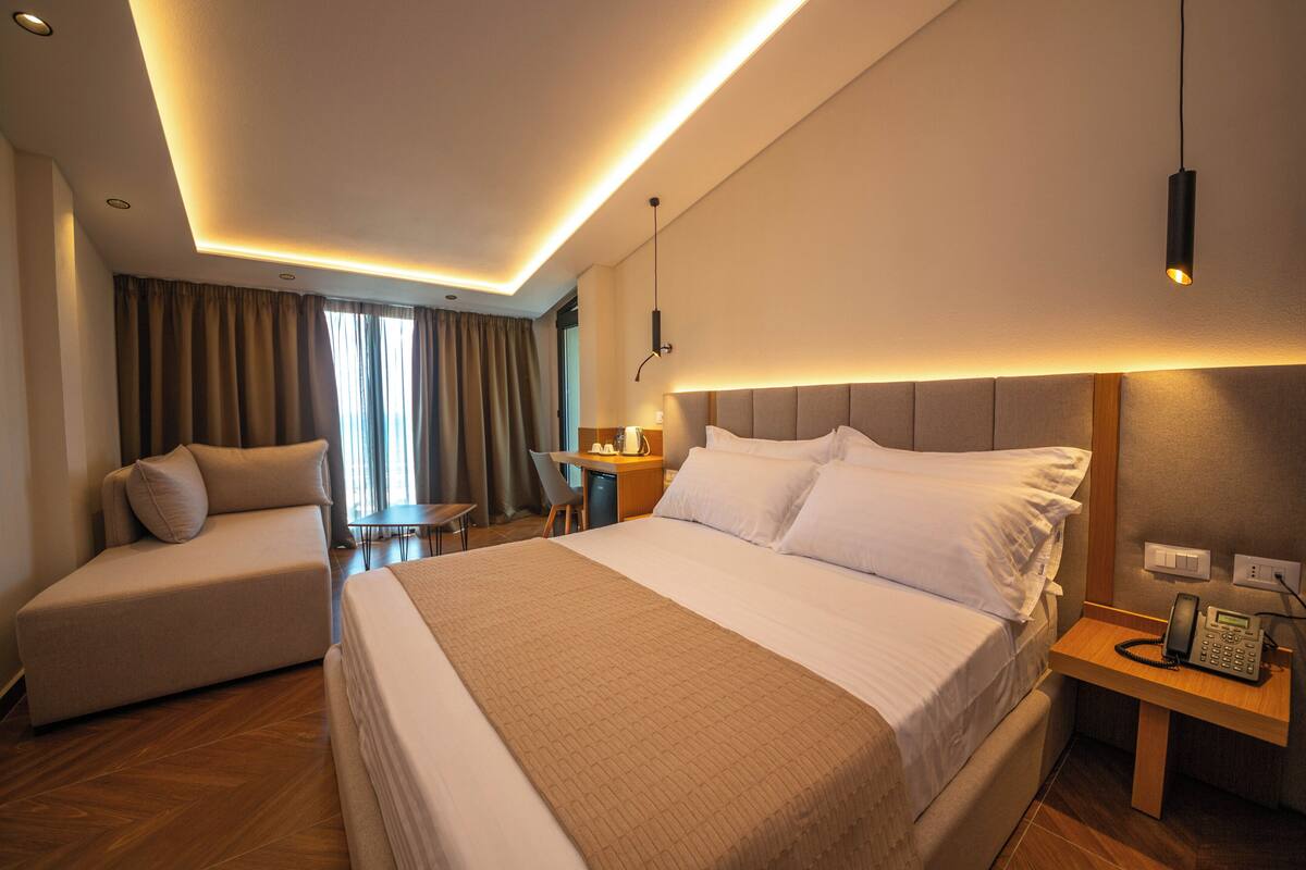 A hotel room with a large bed, a sofa, a desk, and a telephone.