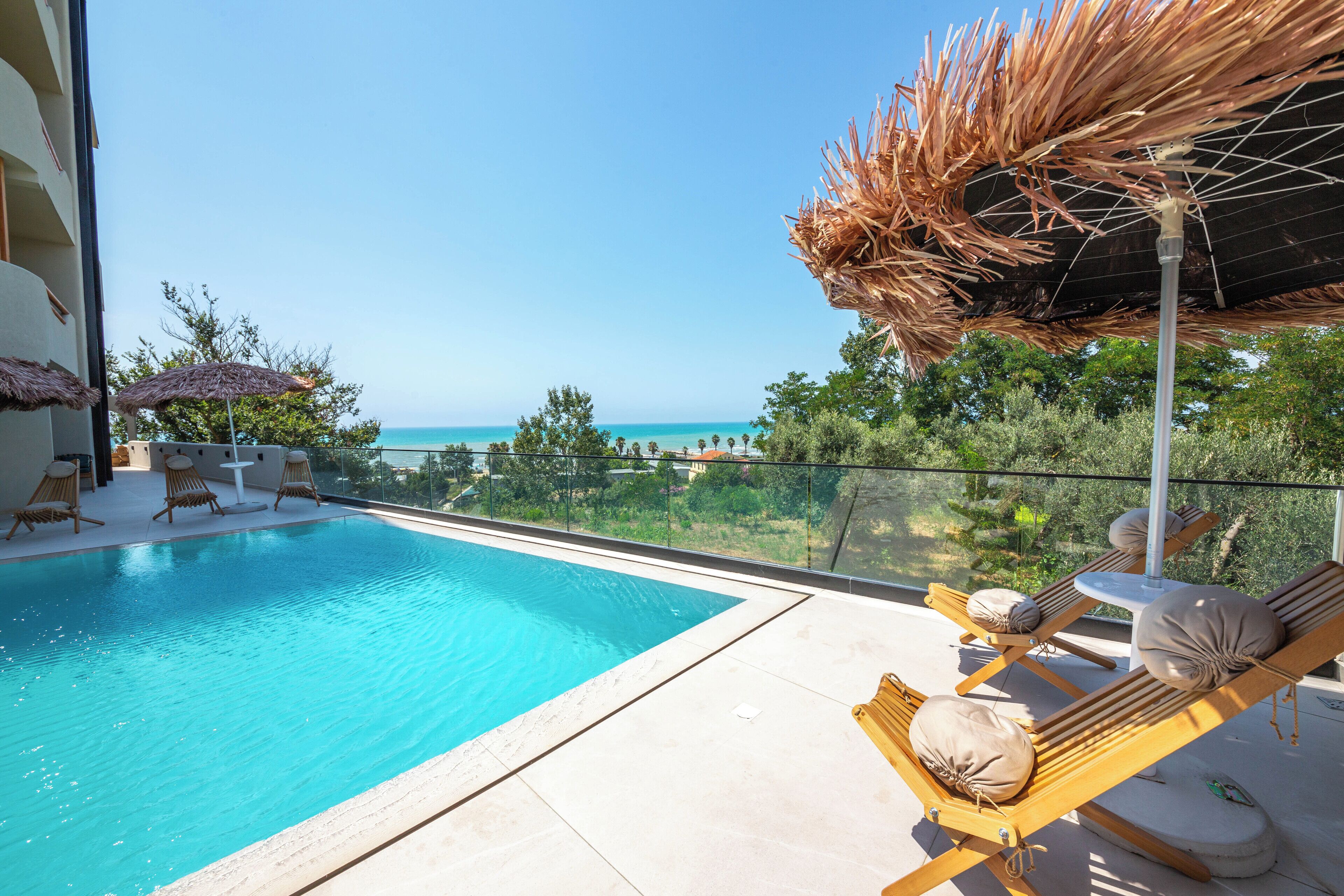 A poolside area with lounge chairs, a thatched umbrella, and a view of the sea.