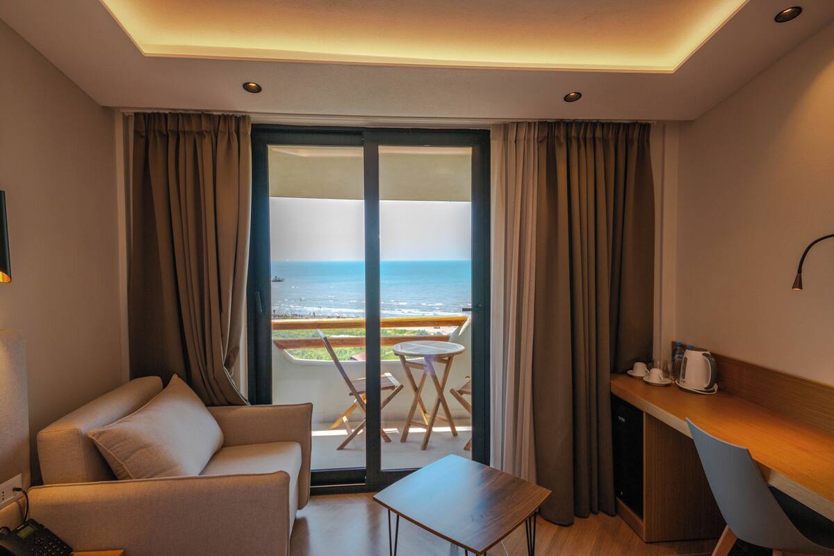 A hotel room with a balcony, a sofa, a small table, and a desk with a chair.