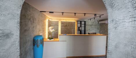 Un espace d’accueil au design moderne, comprenant un comptoir de réception, un vase bleu orné de fleurs et une grande porte en arc de cercle.