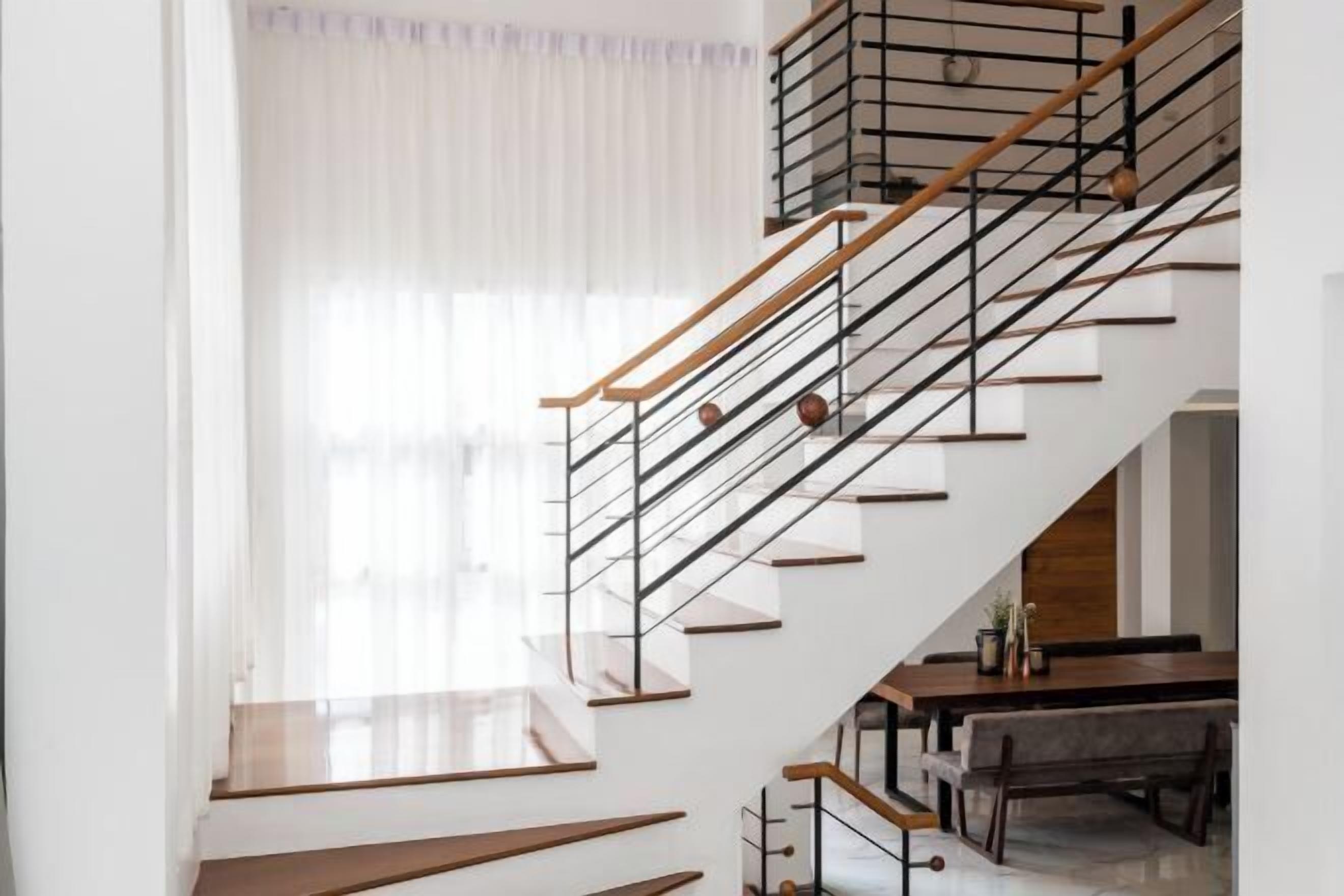 Un escalier moderne avec des marches en bois et des rampes en métal, menant à un coin repas agrémenté d’une table et de chaises en bois.