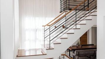 Un escalier moderne avec des marches en bois et des rampes en métal, menant à un coin repas agrémenté d’une table et de chaises en bois.