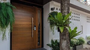 A modern building entrance with a wooden door, potted plants, and a concrete pathway. - Nimman villa 17 @Nimman soi17 (Chiang Mai)