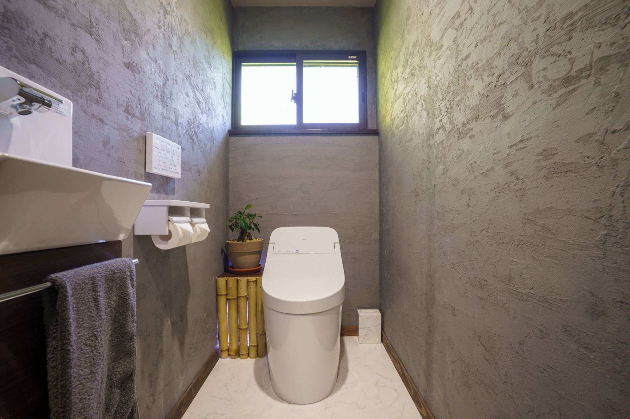 Une petite salle de bain comprenant des toilettes, un lavabo, un miroir, un porte-serviettes, une plante en pot et une fenêtre.