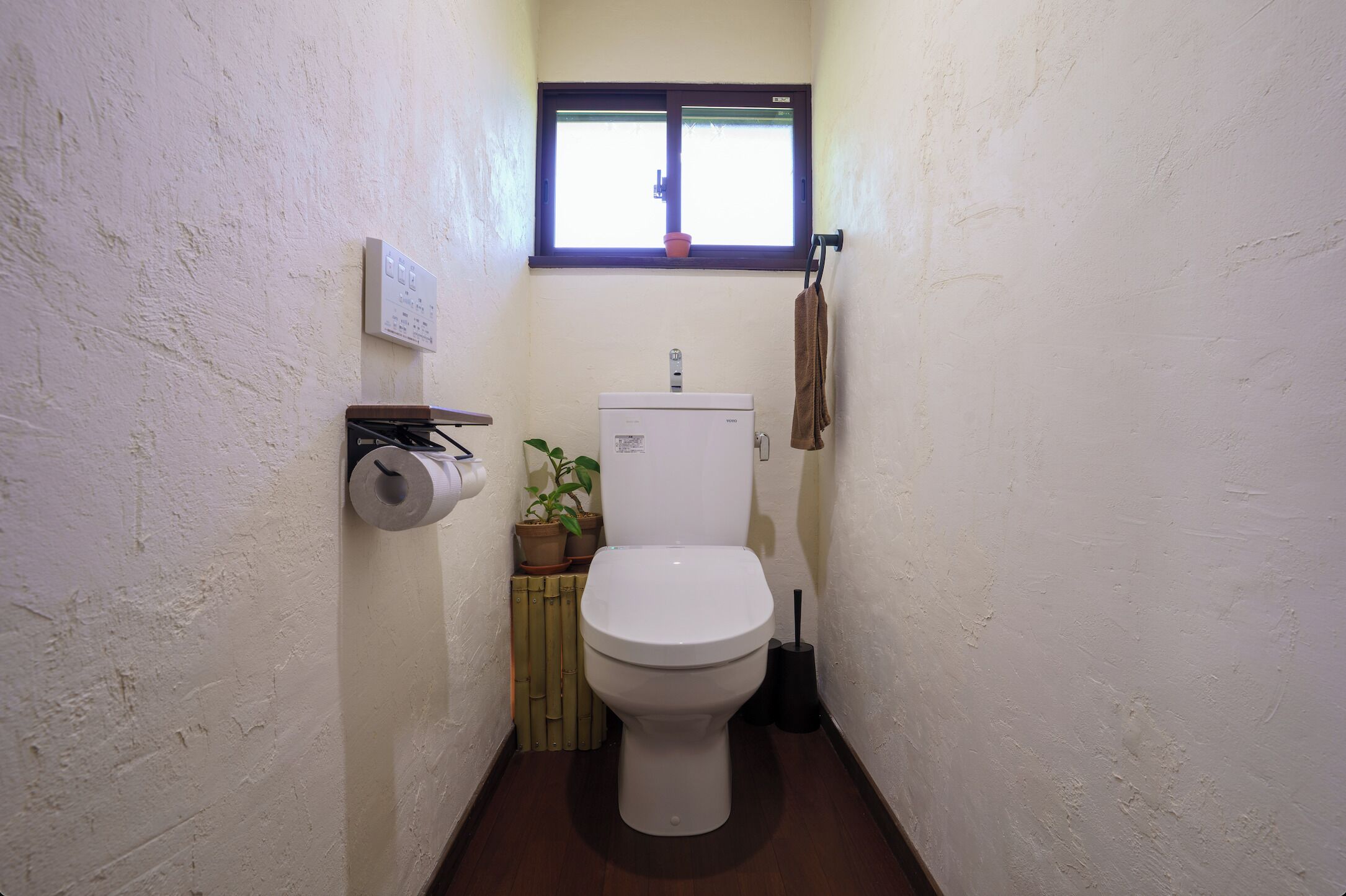 A small bathroom with a toilet, a window, a radiator, and a potted plant.