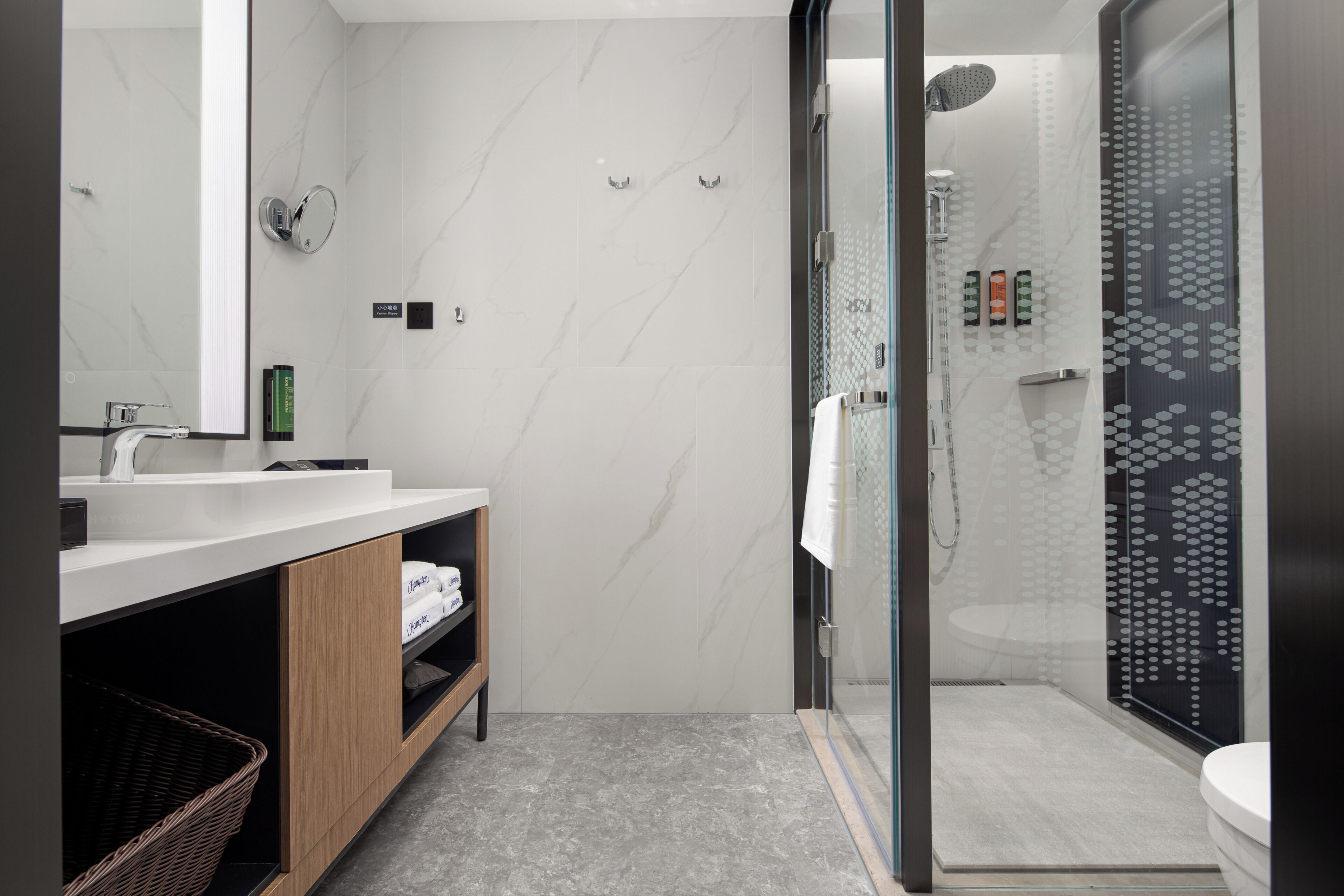 A modern bathroom with a glass shower enclosure, a white sink, and a wooden vanity.