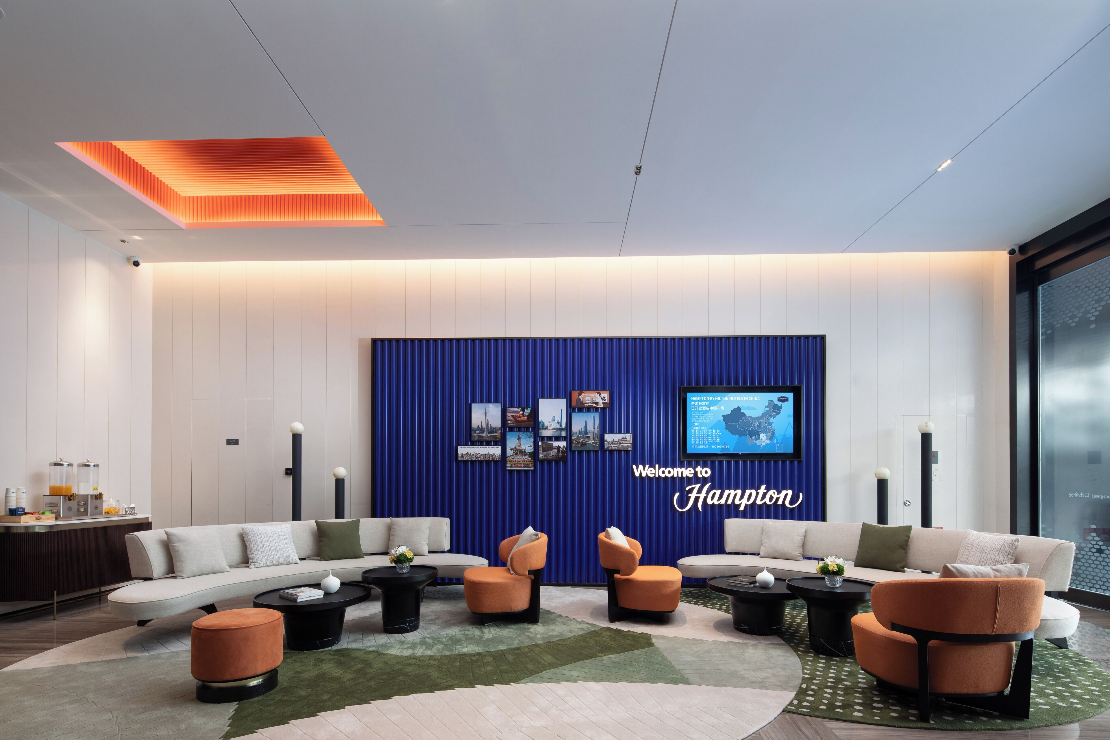 A modern lobby with a blue accent wall, a welcome sign, and a seating area with sofas and armchairs.