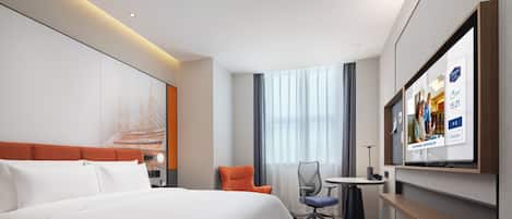 A hotel room with a large bed, a desk, a chair, and a TV mounted on the wall.