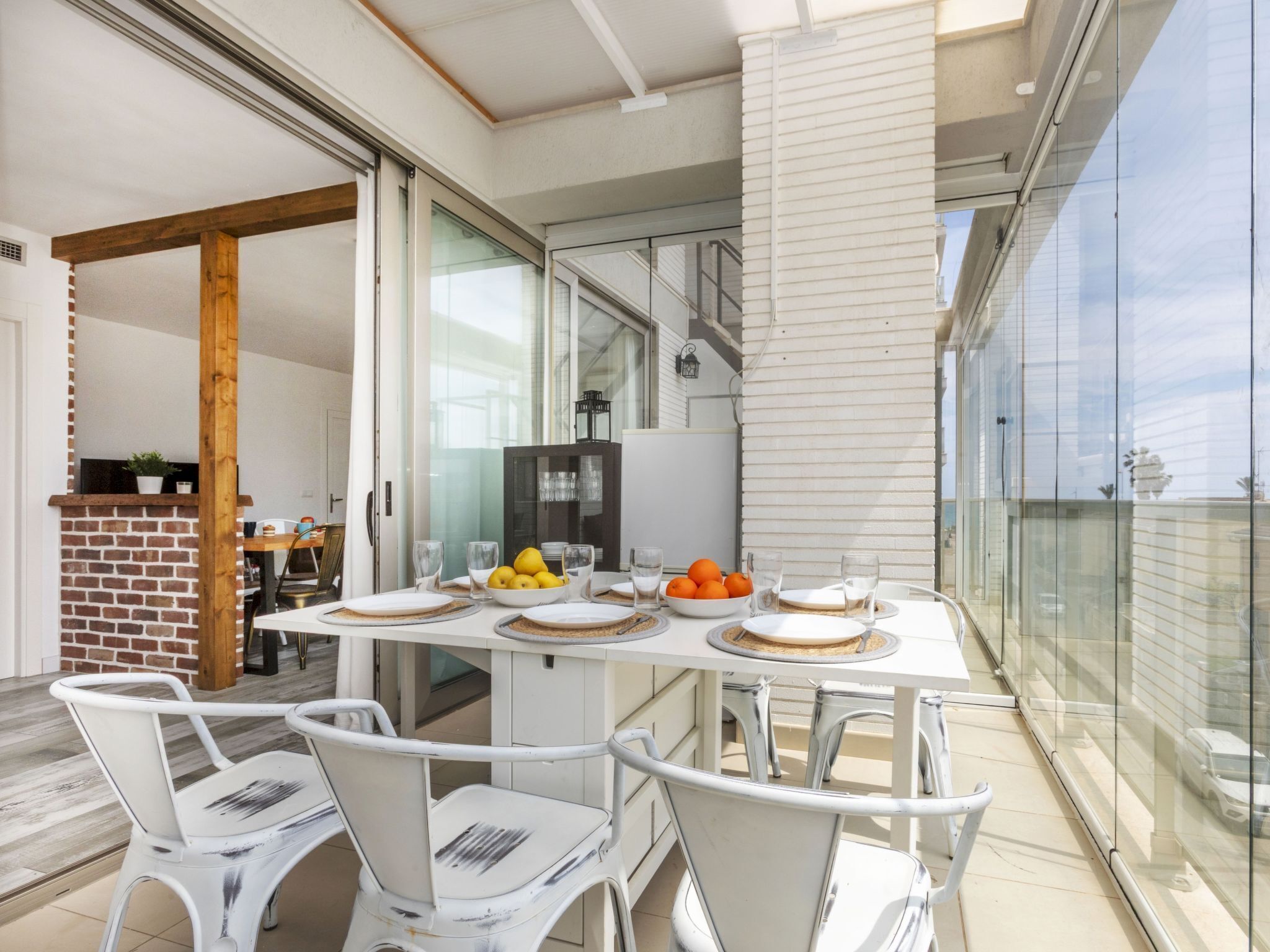 A modern dining area with a glass balustrade, white furniture, and a view of the city.