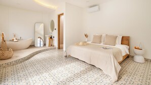 Een moderne slaapkamer met een groot bed, een ingebouwd bad en een klein zithoekje met een spiegel en een kruk.