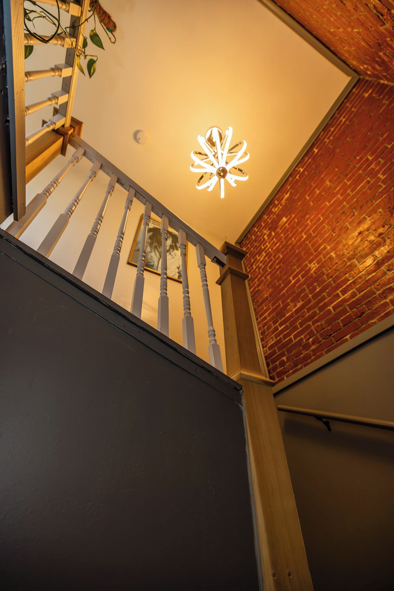 A staircase with a white railing, a brick wall, and a ceiling light fixture.