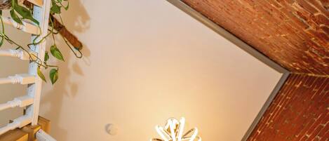 A staircase with white balusters and a wooden handrail, leading to a room with a brick wall and a ceiling light fixture.