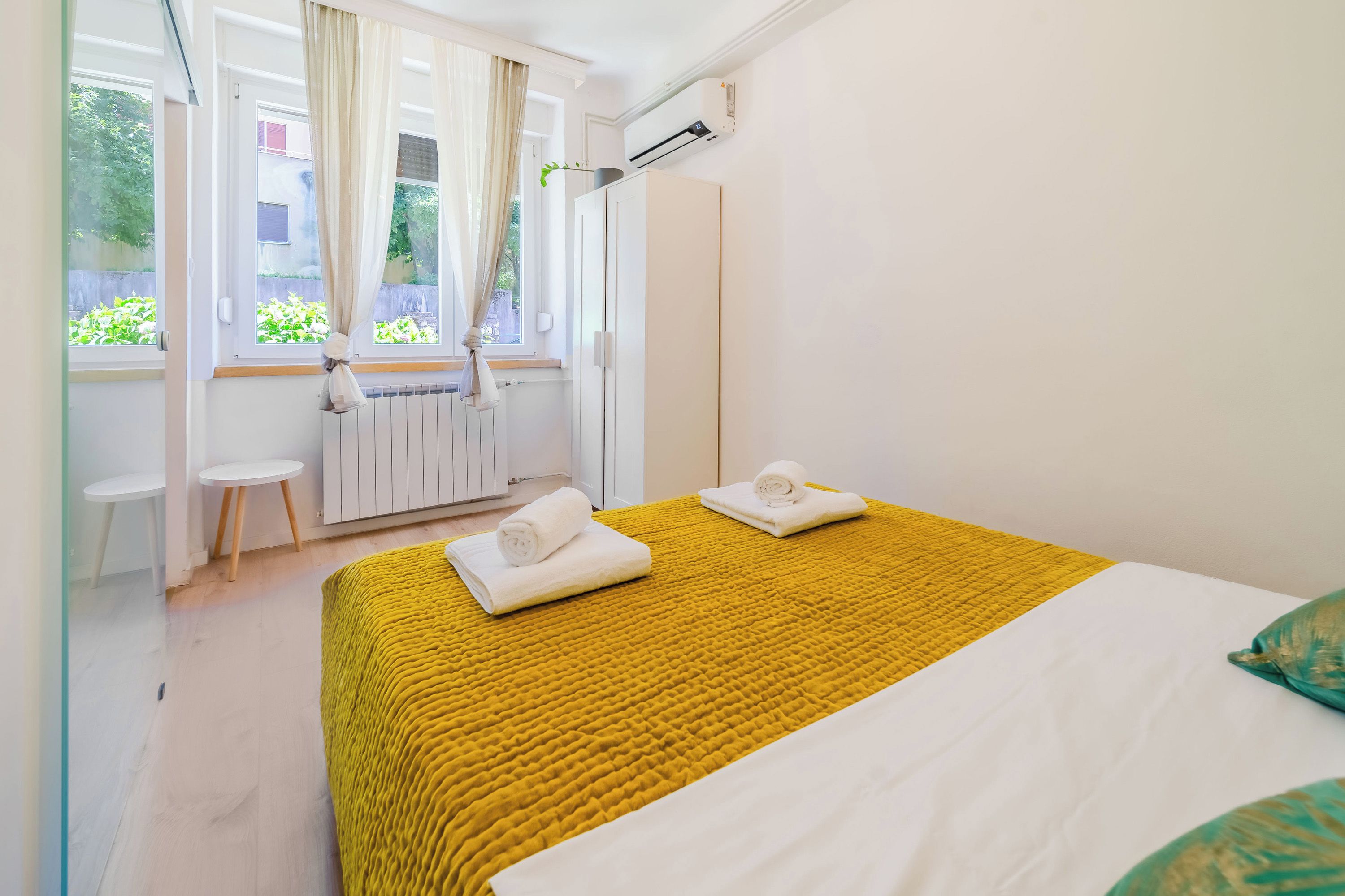 Quarto de hotel com uma cama, duas cadeiras, um radiador e uma janela com cortinas.