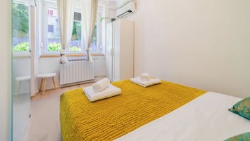Quarto de hotel com uma cama, duas cadeiras, um radiador e uma janela com cortinas.