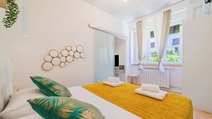 Une chambre d’hôtel avec un lit, des oreillers, une couvre-lit jaune à motifs, une œuvre d’art murale et une fenêtre avec des rideaux.