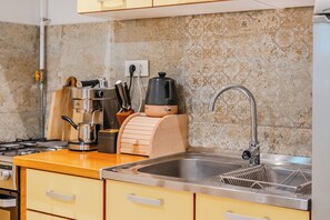 Uma cozinha com uma pia de aço inoxidável, uma cafeteira, um bule e um aparador de pão de madeira.