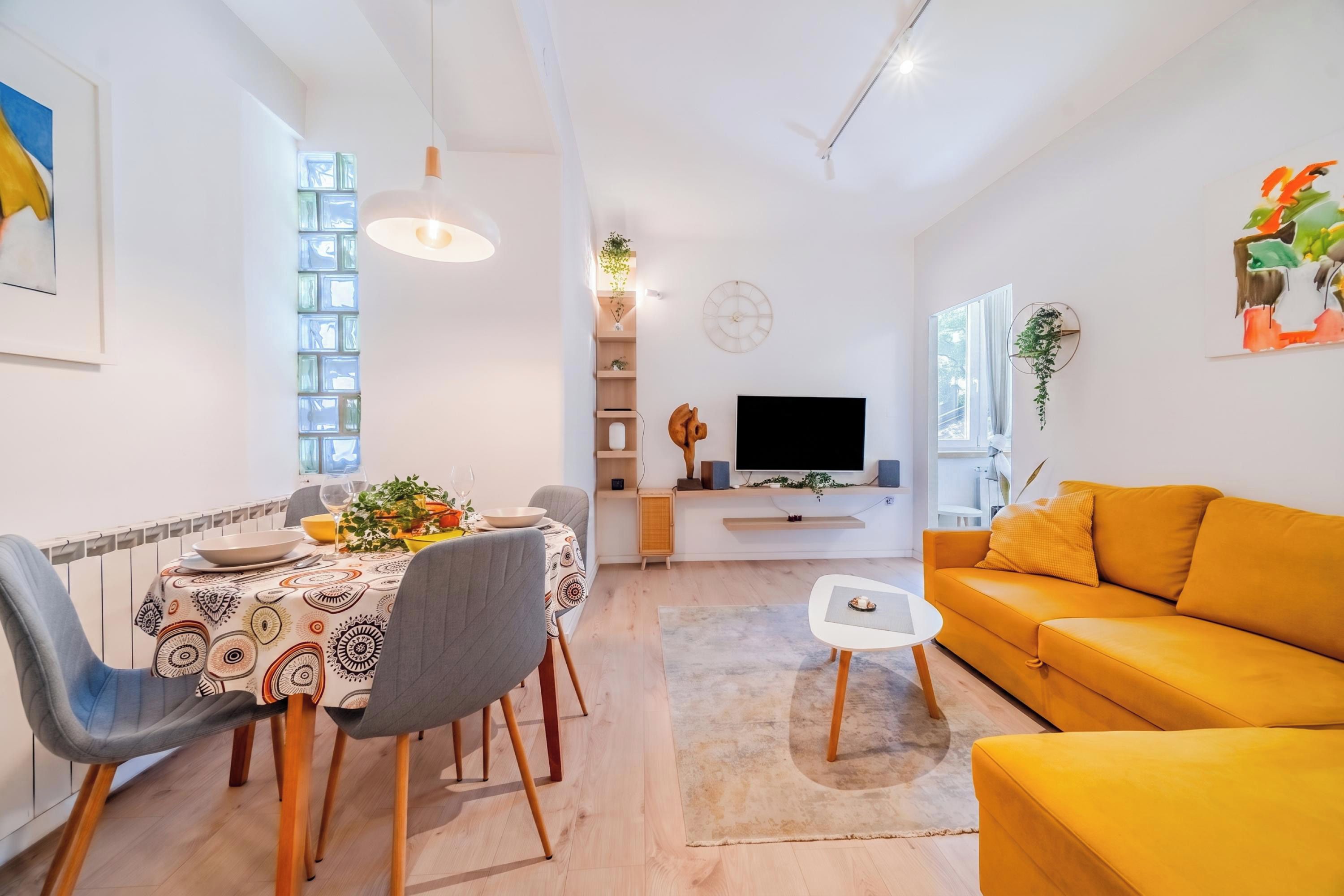 Een moderne woonkamer met een eethoek, een bank, een televisie en een plant.